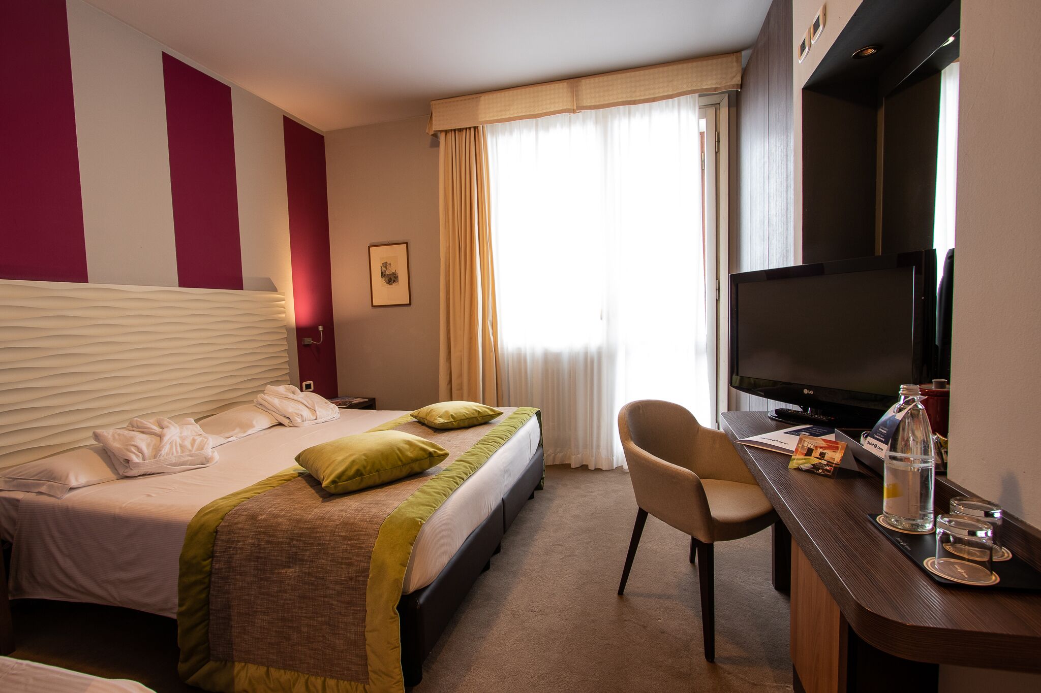 Una habitación de hotel con cama, escritorio con televisor y una silla.