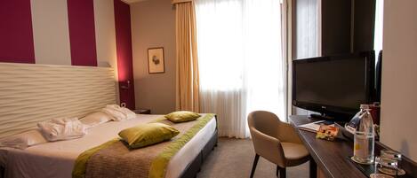 Una habitación de hotel con cama, escritorio con televisor y una silla.