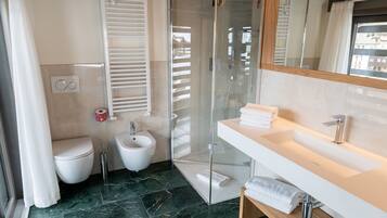 A modern bathroom with a glass-enclosed shower, a bidet, a toilet, and a vanity with a mirror.