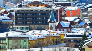 A snow-covered village with colorful buildings, including a prominent red and yellow structure with a steep roof. - Hotel Cristallo Club (Corteno Golgi)