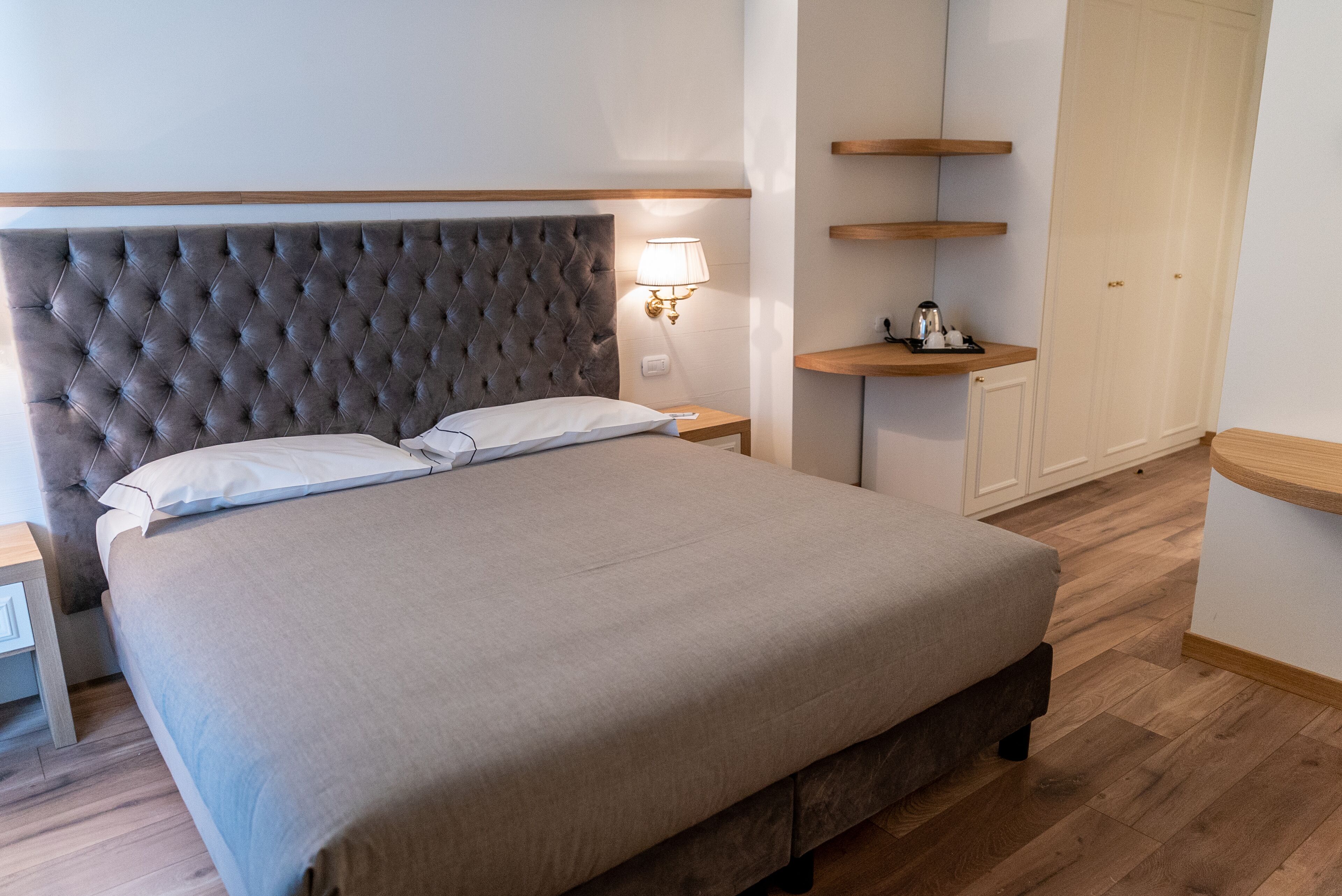 Uma cama bem arrumada com cabeceira estofada, mesa de cabeceira com abajur e estantes de madeira.