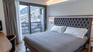 A hotel room with a large bed, a wooden desk, a chair, a balcony with a view of snow-covered hills. - Hotel Cristallo Club (Corteno Golgi)