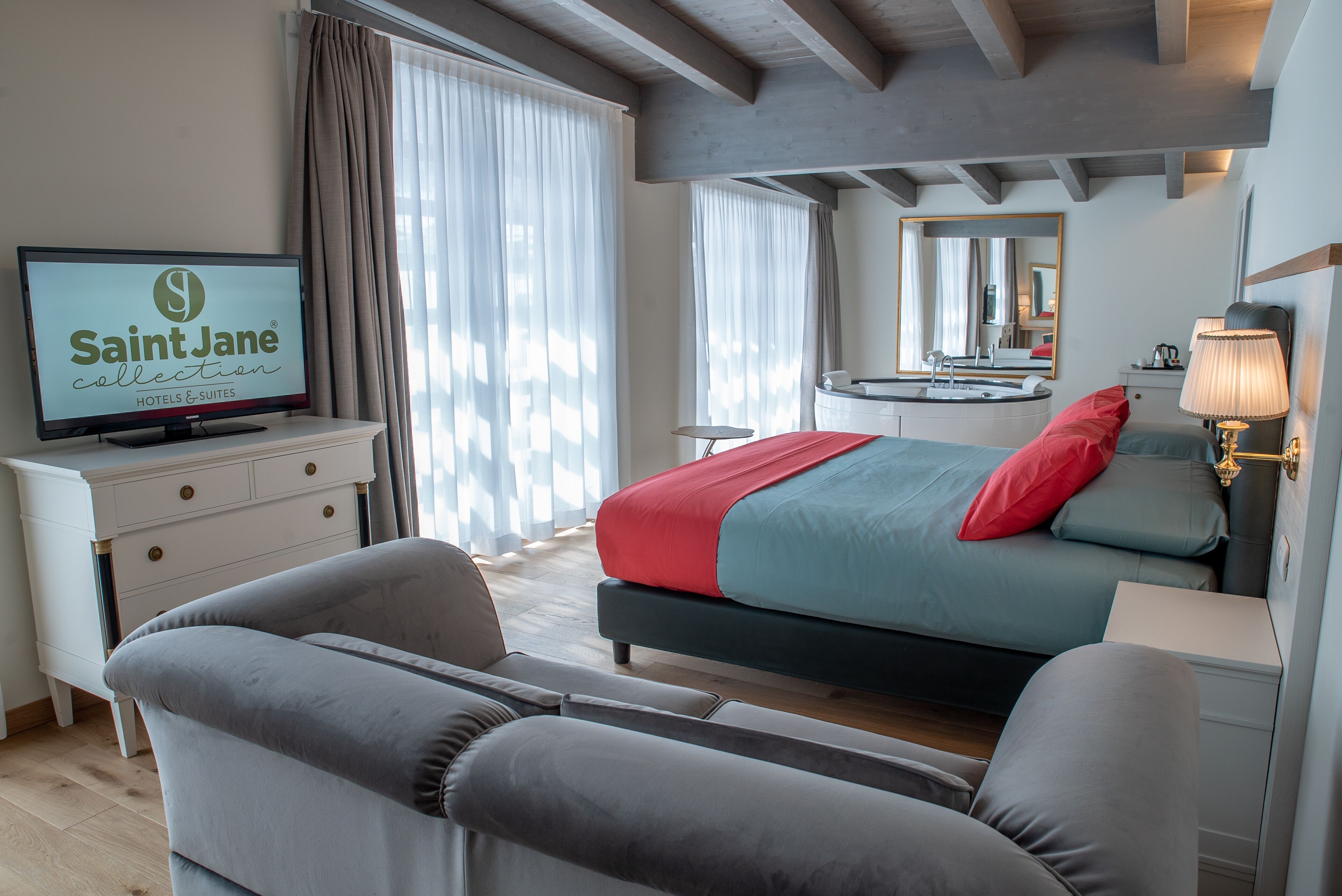 A modern hotel room with a bed, a television, a desk, and a mirror.