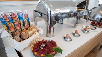A buffet setup with various food items, including bread, pastries, and a dish with meat and eggs.