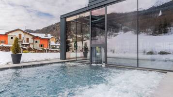 Um edifício moderno com fachada de vidro, área de piscina com gelo e paisagem nevada com casas ao fundo.
