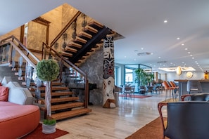 A modern hotel lobby with a wooden staircase, a round seating area, and a reception desk. - Cristallo Wellness Hotel (Corteno Golgi)