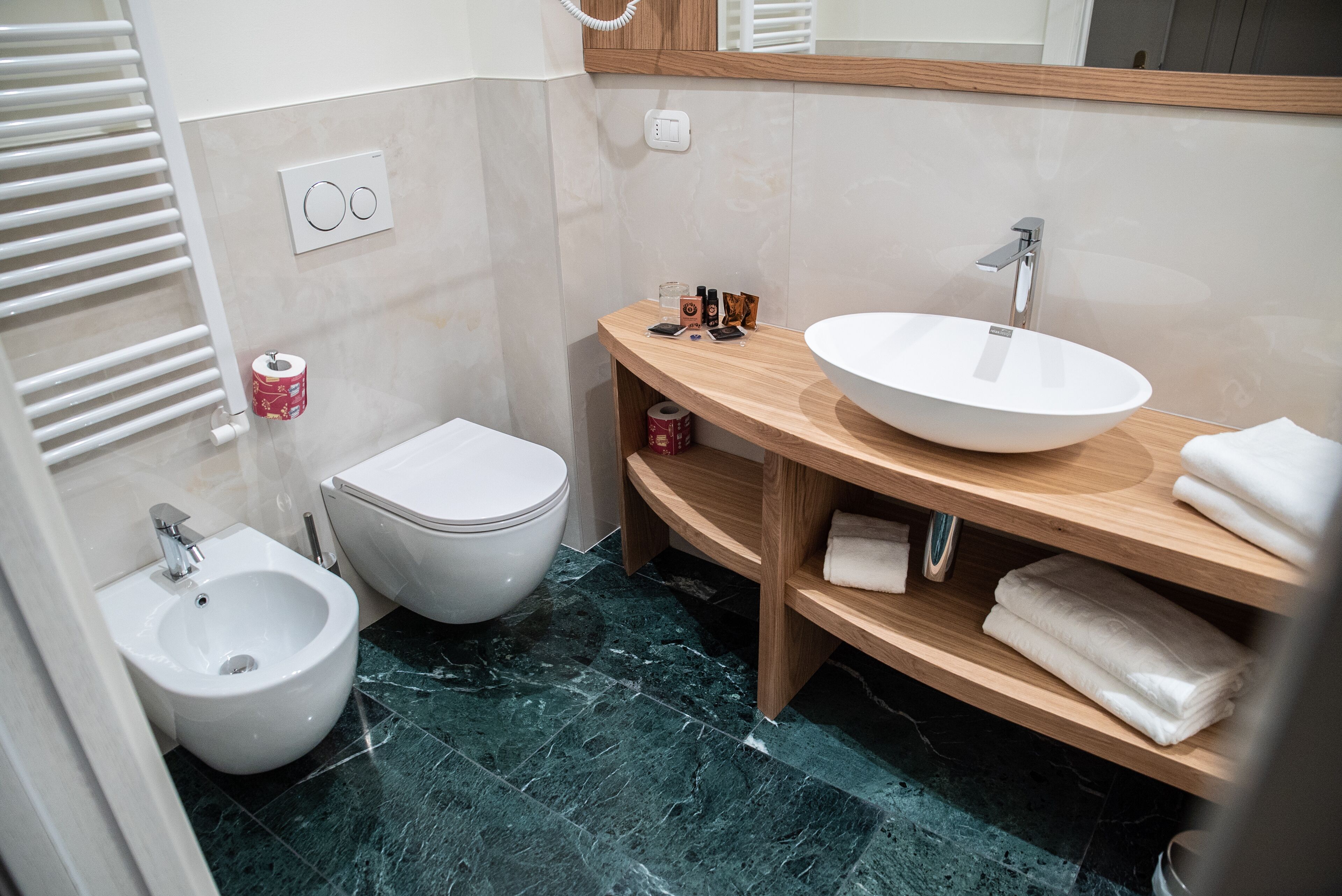 Un baño moderno con bidé, inodoro y un lavamanos grande con espejo.