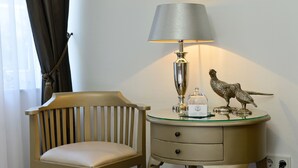 A room with a wooden chair, a bedside table with a lamp, and a decorative bird statue.