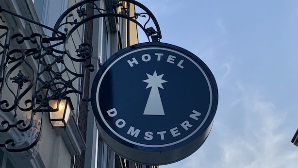 A circular sign with "HOTEL DOMSTERN" and a star symbol, mounted on a building with a no parking sign below.