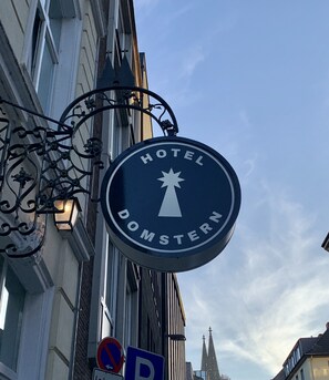 A circular sign with "HOTEL DOMSTERN" and a star symbol, mounted on a building with a no parking sign below. - Hotel Domstern (Cologne)