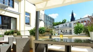 A modern outdoor seating area with wicker furniture and a glass table, overlooking a cityscape with historic buildings.