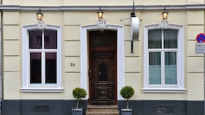 A building with a large wooden door, three windows with white frames, and two small potted plants.