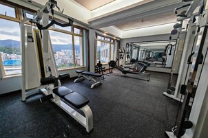 Un gimnasio con equipo de ejercicio, ventanas amplias y vista a la ciudad.