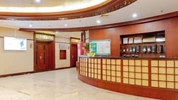 A hotel reception area with a wooden reception desk, a bulletin board, and framed certificates.