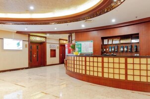 Zona de recepción de hotel con un mostrador de madera, un tablón de anuncios y certificados enmarcados.