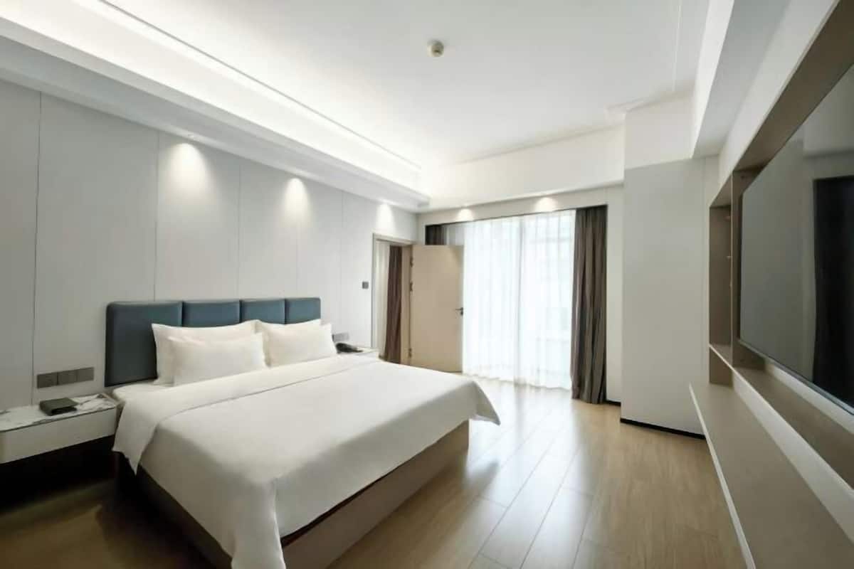 Una habitación de hotel moderna con una cama grande, mesitas de noche, un televisor y una puerta corredera a un balcón.