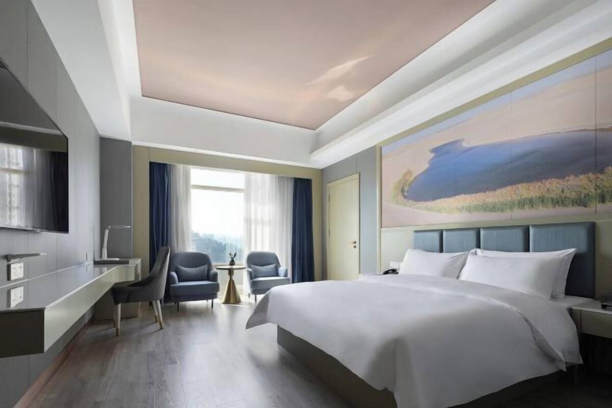 Habitación de hotel con cama, escritorio, silla, televisión y un cuadro en la pared.