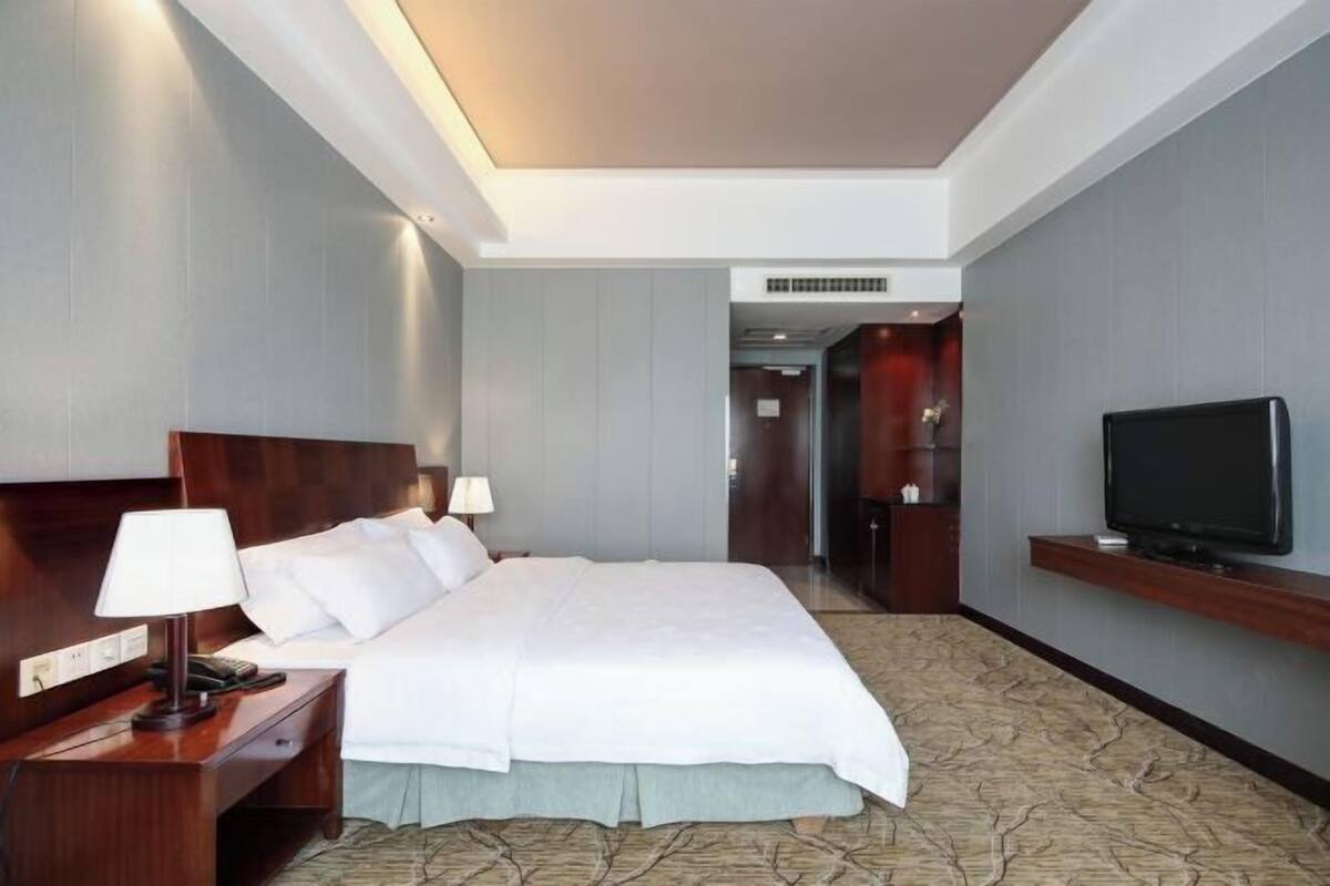 Habitación de hotel con una cama grande, mesitas de noche, un televisor y vistas al pasillo.