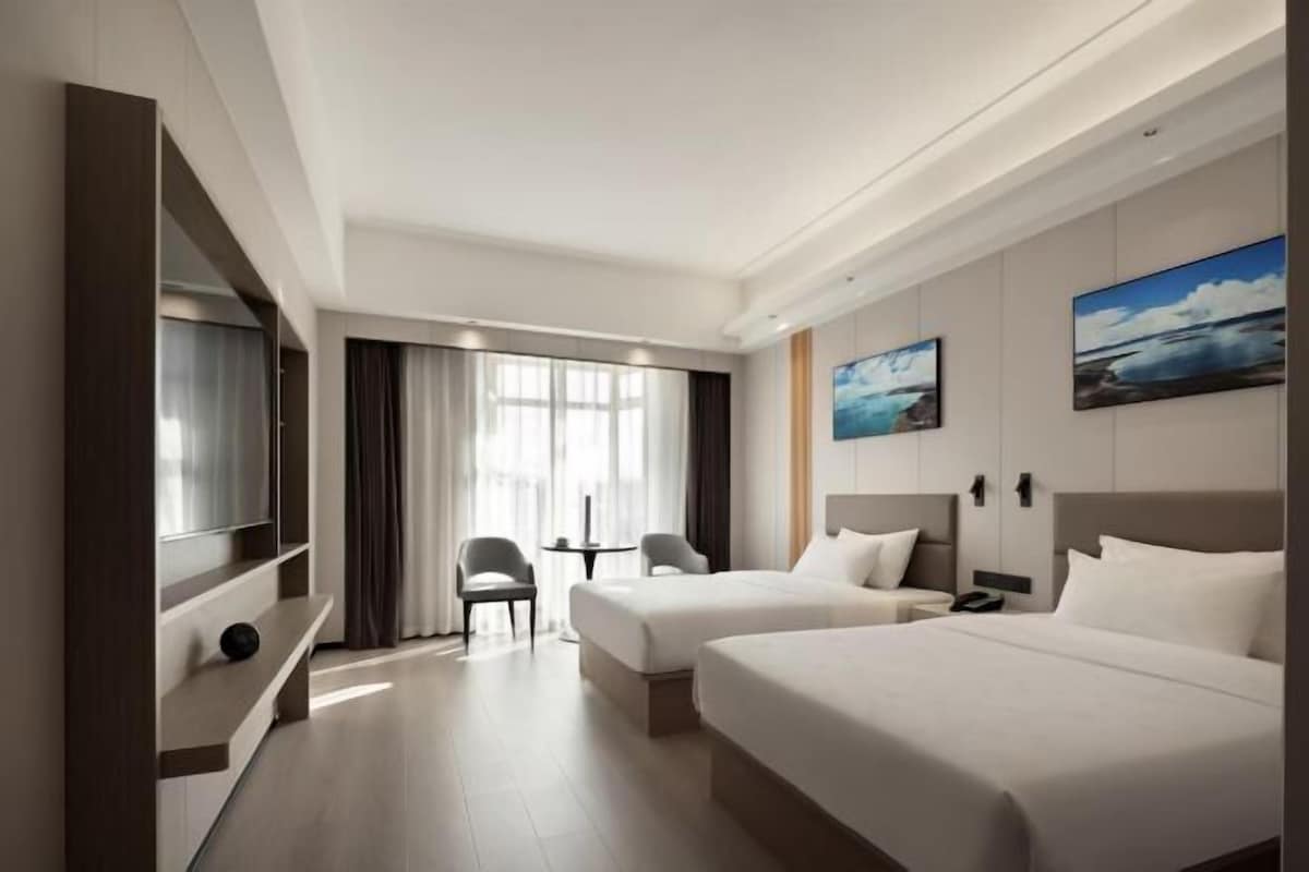 A hotel room with two beds, a TV, a desk, and a chair.