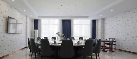 Un salón de conferencias con una mesa larga, sillas y un televisor en la pared.