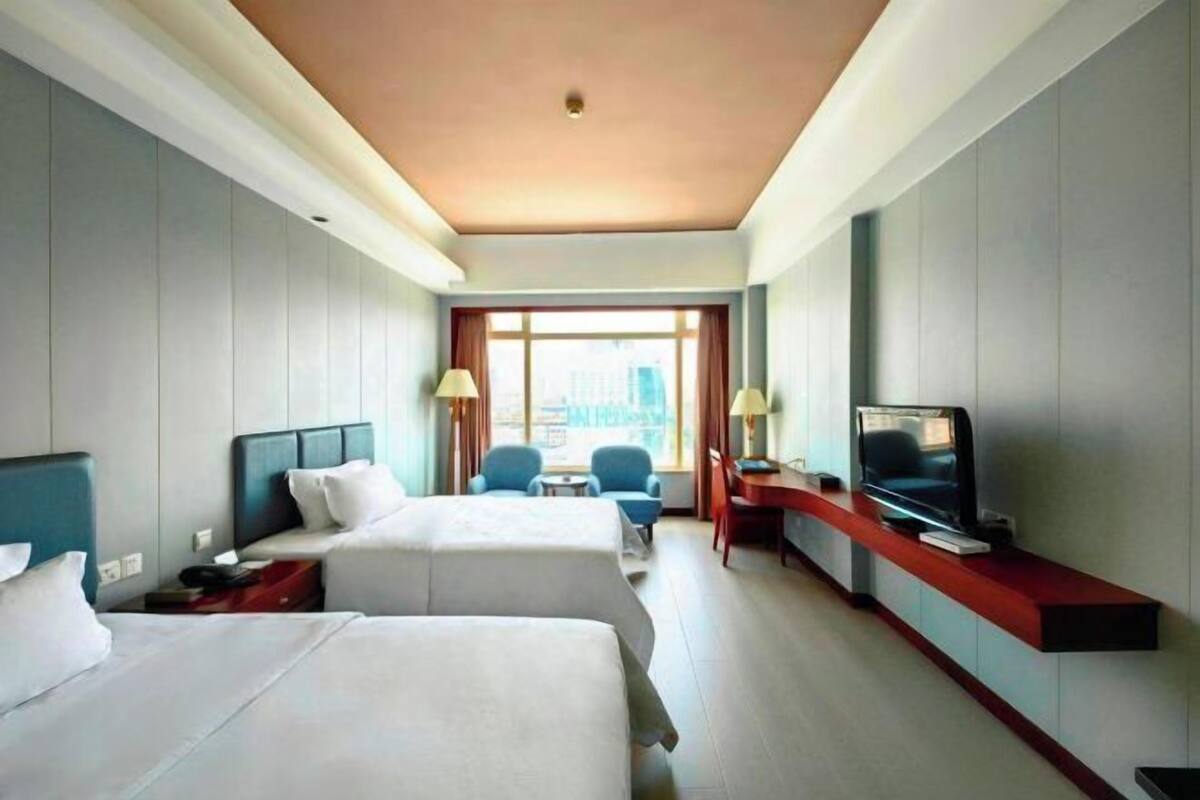 Une chambre d’hôtel avec deux lits, une télévision, un bureau et une fenêtre donnant sur la ville.