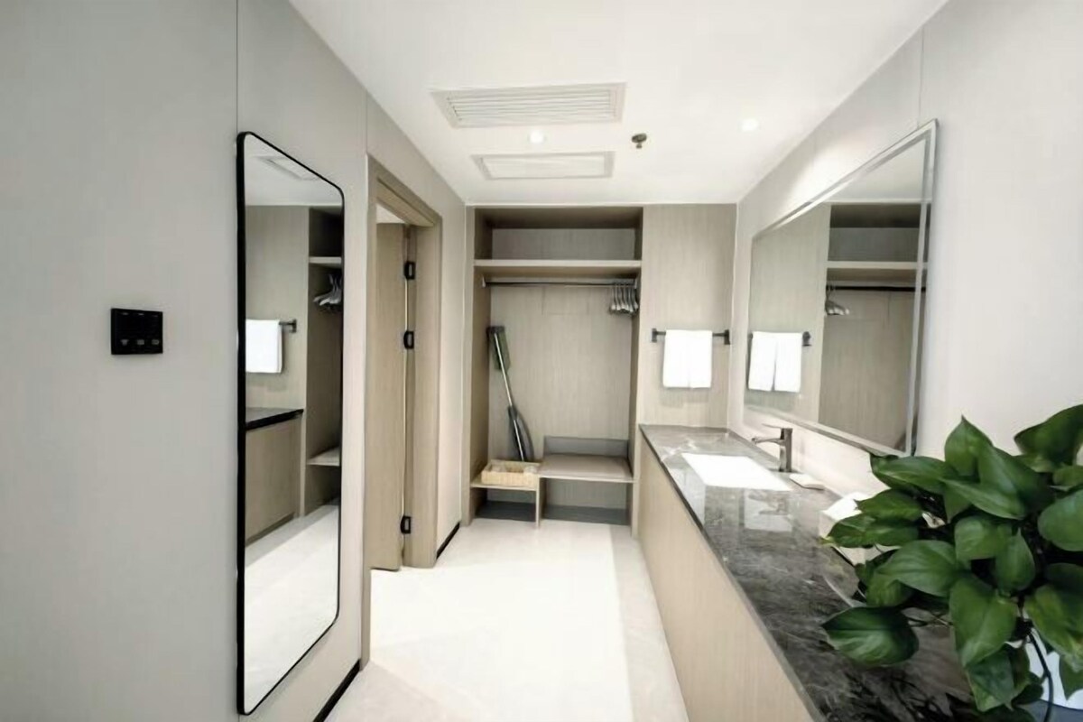 A modern bathroom with a large mirror, a sink, a shower, and a walk-in closet.