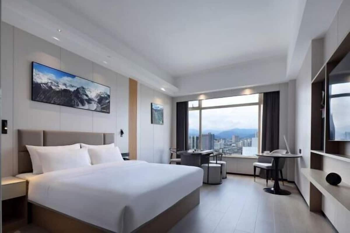 Una habitación de hotel moderna con una cama grande, un escritorio, una silla y vistas a la ciudad.