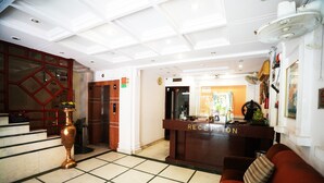 A hotel reception area with a reception desk, a sofa, a staircase, and a large vase. - Hotel Classic Karol Bagh (New Delhi)