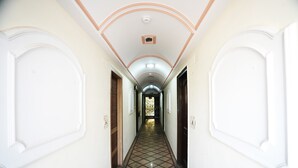 A long, narrow hallway with white walls and a tiled floor, leading to a door at the end. - Hotel Classic Karol Bagh (New Delhi)