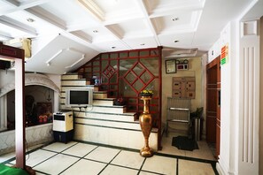 A hotel lobby with a staircase, a large vase, a television, and a security camera. - Hotel Classic Karol Bagh (New Delhi)