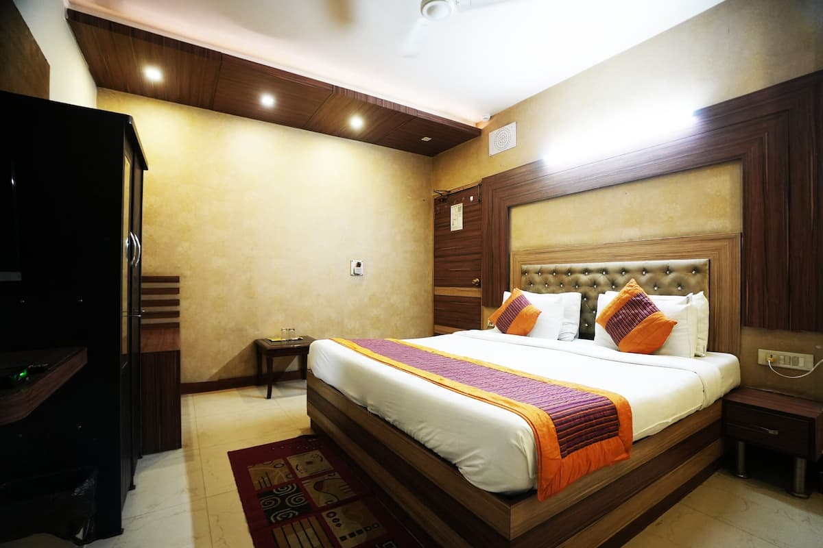 Habitación de hotel bien iluminada con una cama grande, cabecera de madera y una mesita de noche pequeña.