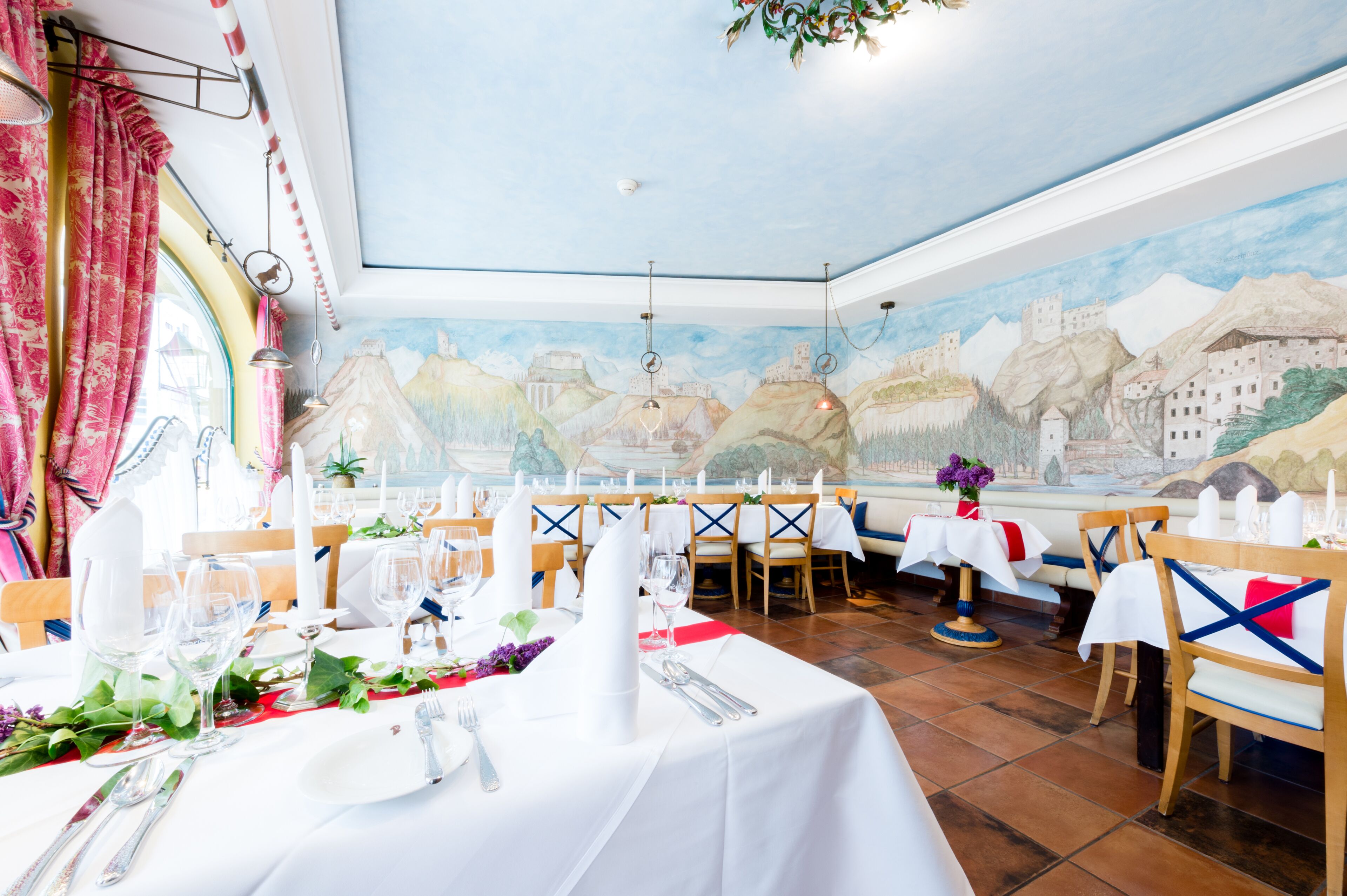 A dining area with tables set for a meal, featuring a mural on the wall depicting a mountainous landscape.