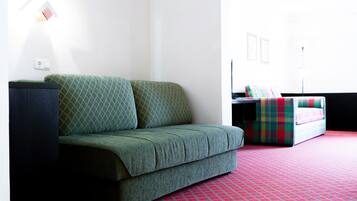 A room with a green sofa, a red patterned carpet, and a small table with a lamp.