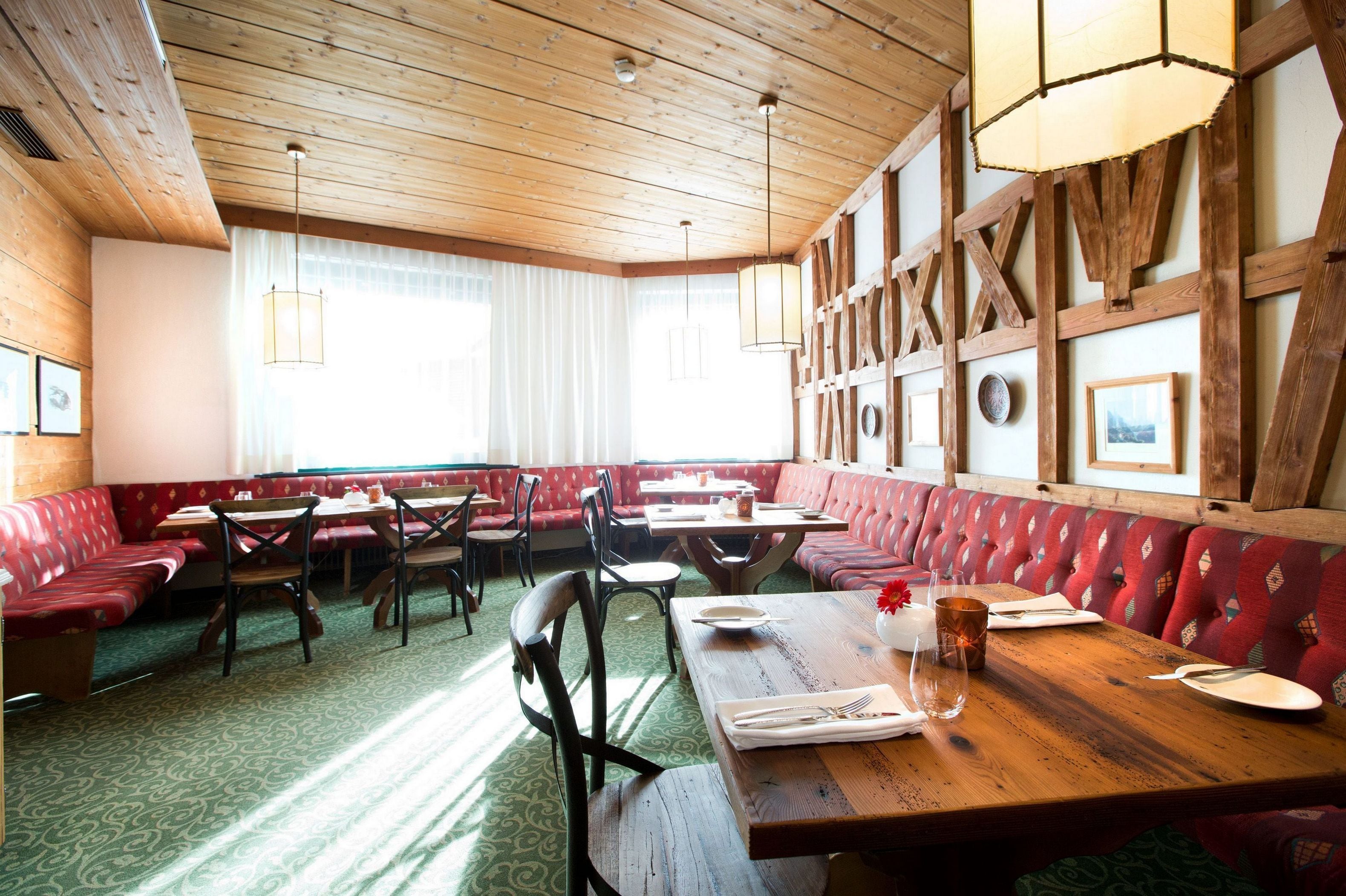 A restaurant with wooden beams, red upholstered booths, and green patterned carpet.