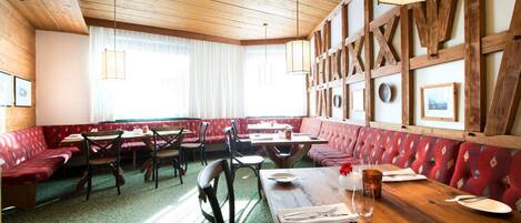 A restaurant with wooden beams, red upholstered booths, and green patterned carpet.