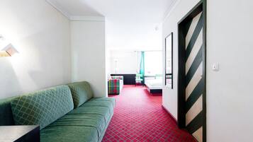 A hotel corridor with a green sofa, a red carpet, and a bed with a striped headboard.