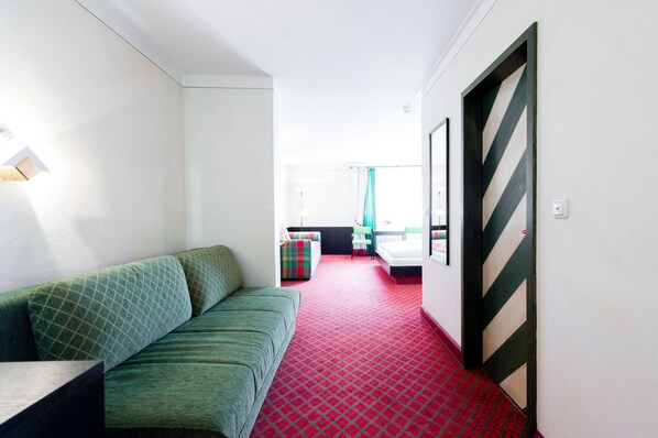 A hotel corridor with a green sofa, a red carpet, and a bed with a striped headboard.