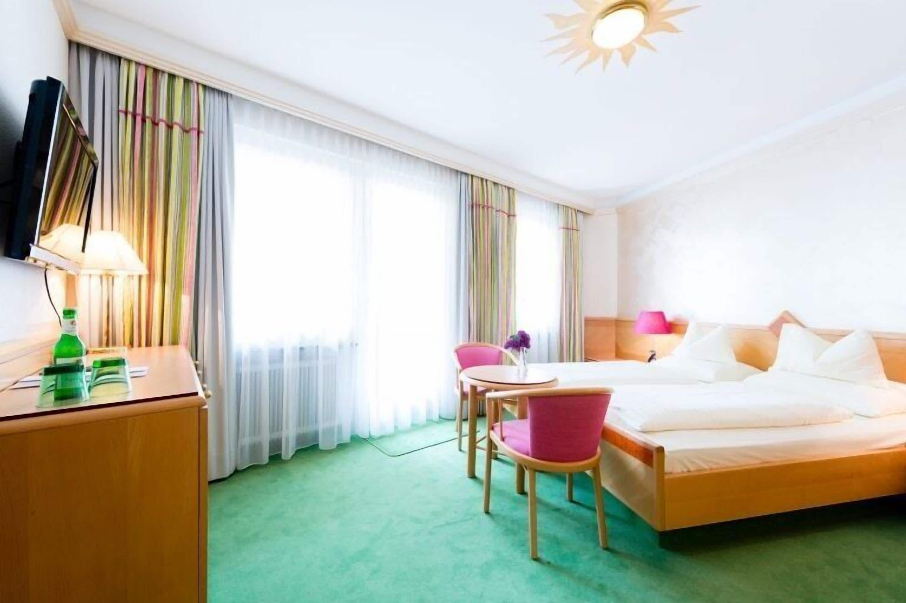 A hotel room with a bed, a desk, a chair, a TV, and a window with curtains.