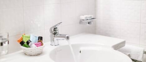 A bathroom sink with a glass bowl containing toiletries, a faucet, and a towel rack.