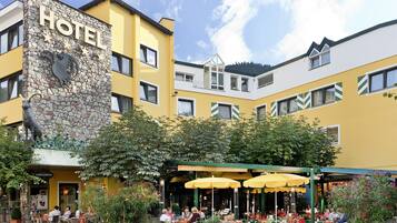 Een hotel met een gevel van steen, een terras met gele parasols, en een bord waarop 'HOTEL' staat.