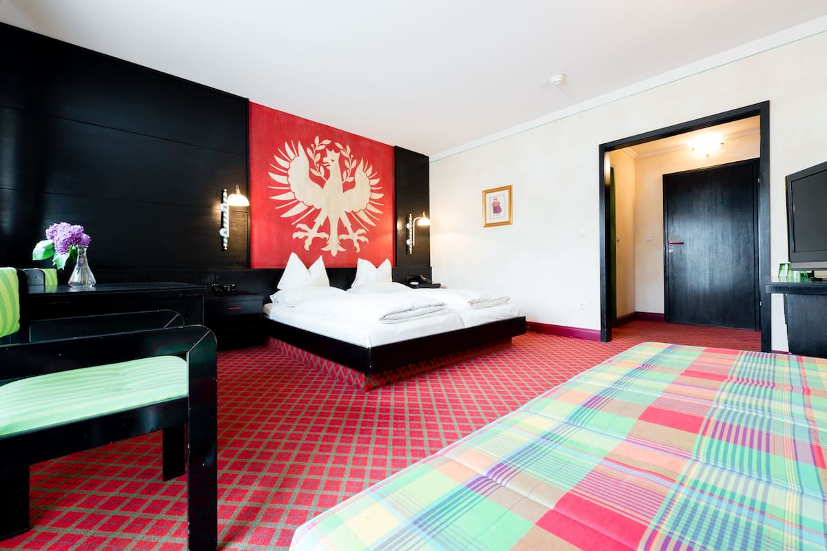 Quarto de hotel com cama, escrivaninha, cadeira, parede vermelha e branca e televisão.