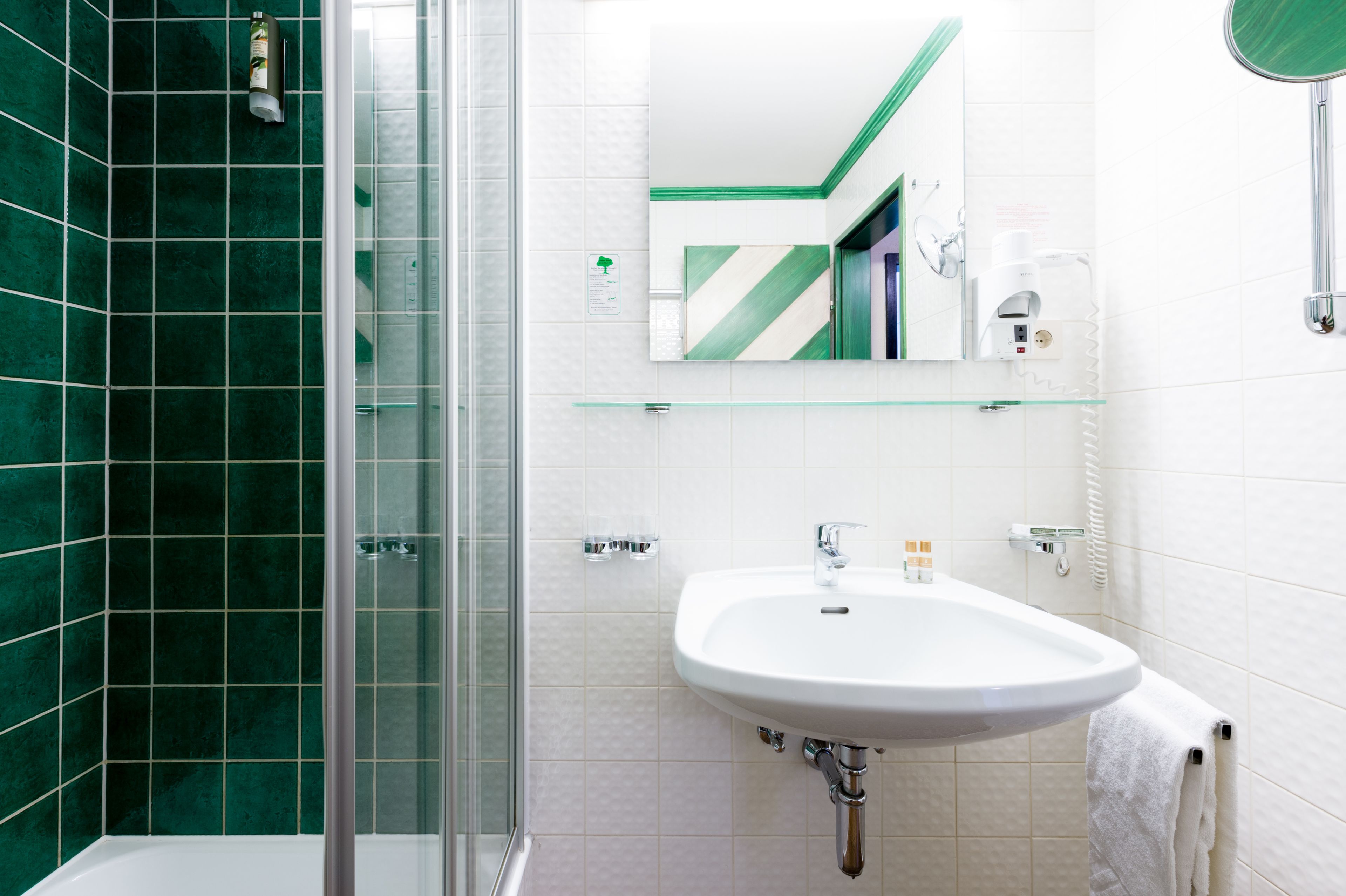 A modern bathroom with a glass shower enclosure, a white sink, and a mirror with a green and white pattern.