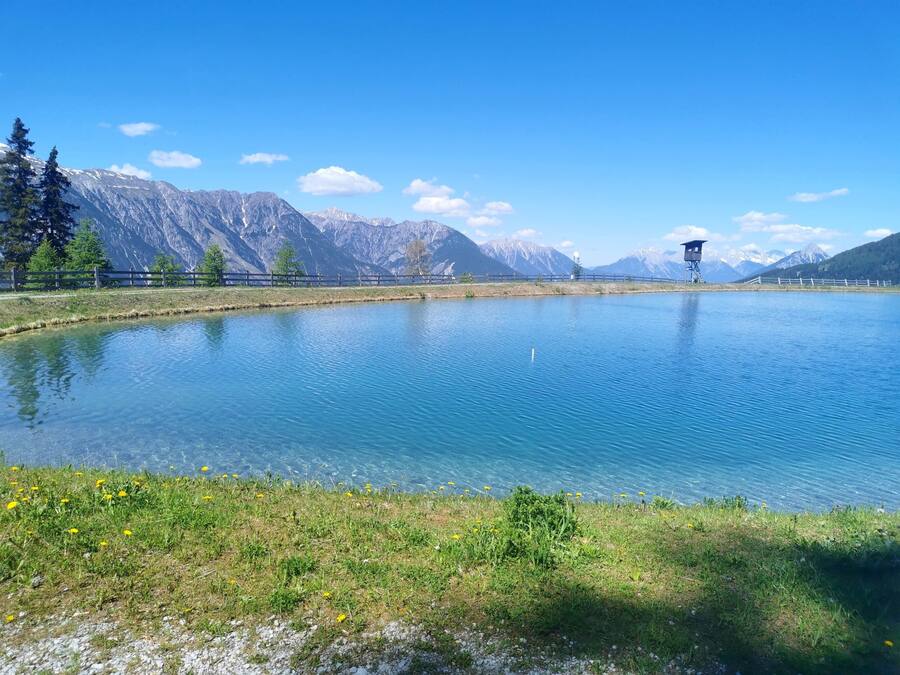 A clear lake with mountains in the background, a wooden fence, and a watchtower.