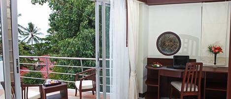 Un balcon avec une porte-fenêtre coulissante, un bureau en bois, une chaise et un ordinateur portable.