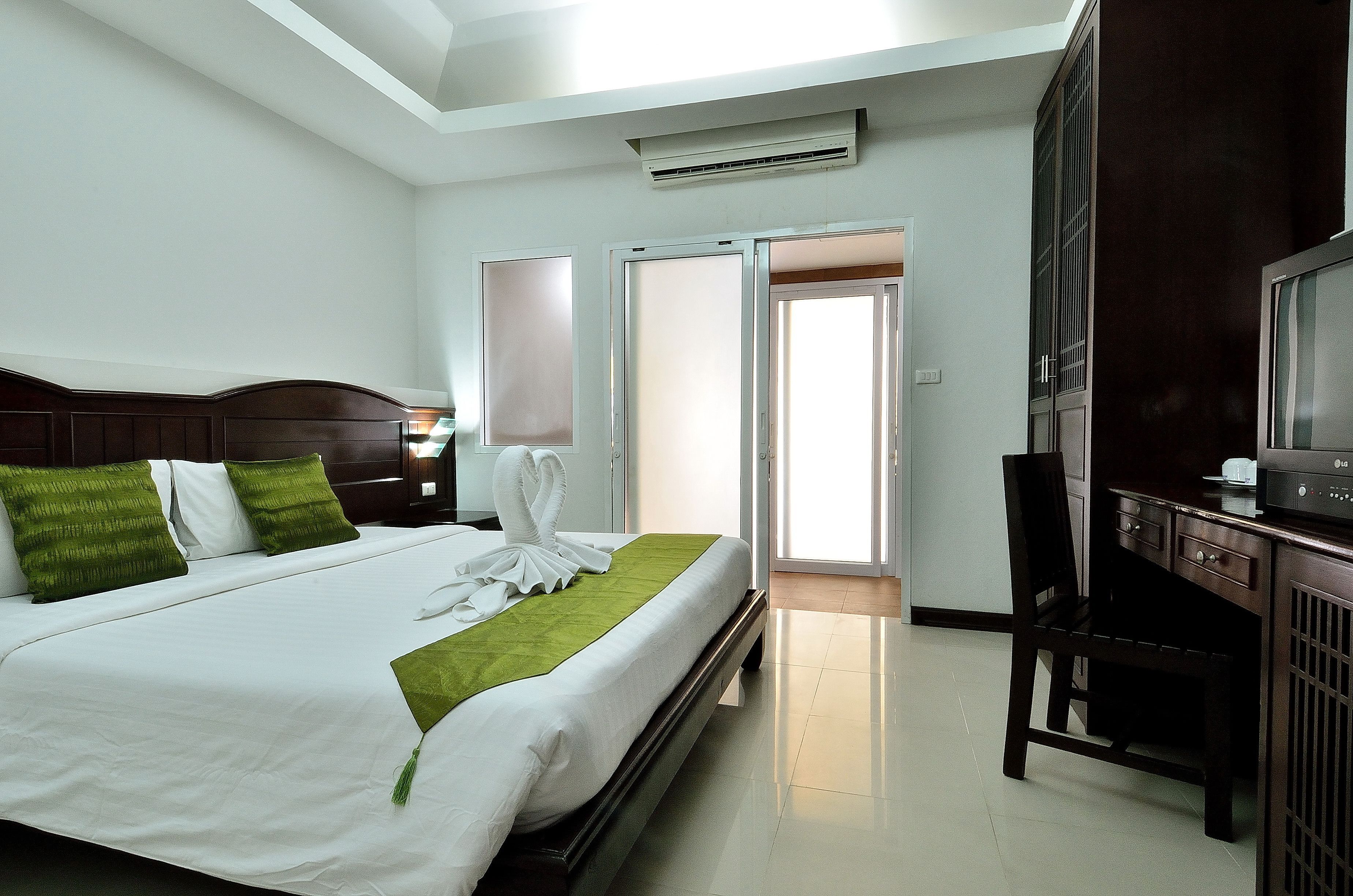 A hotel room with a neatly made bed, a desk with a chair, and a television.
