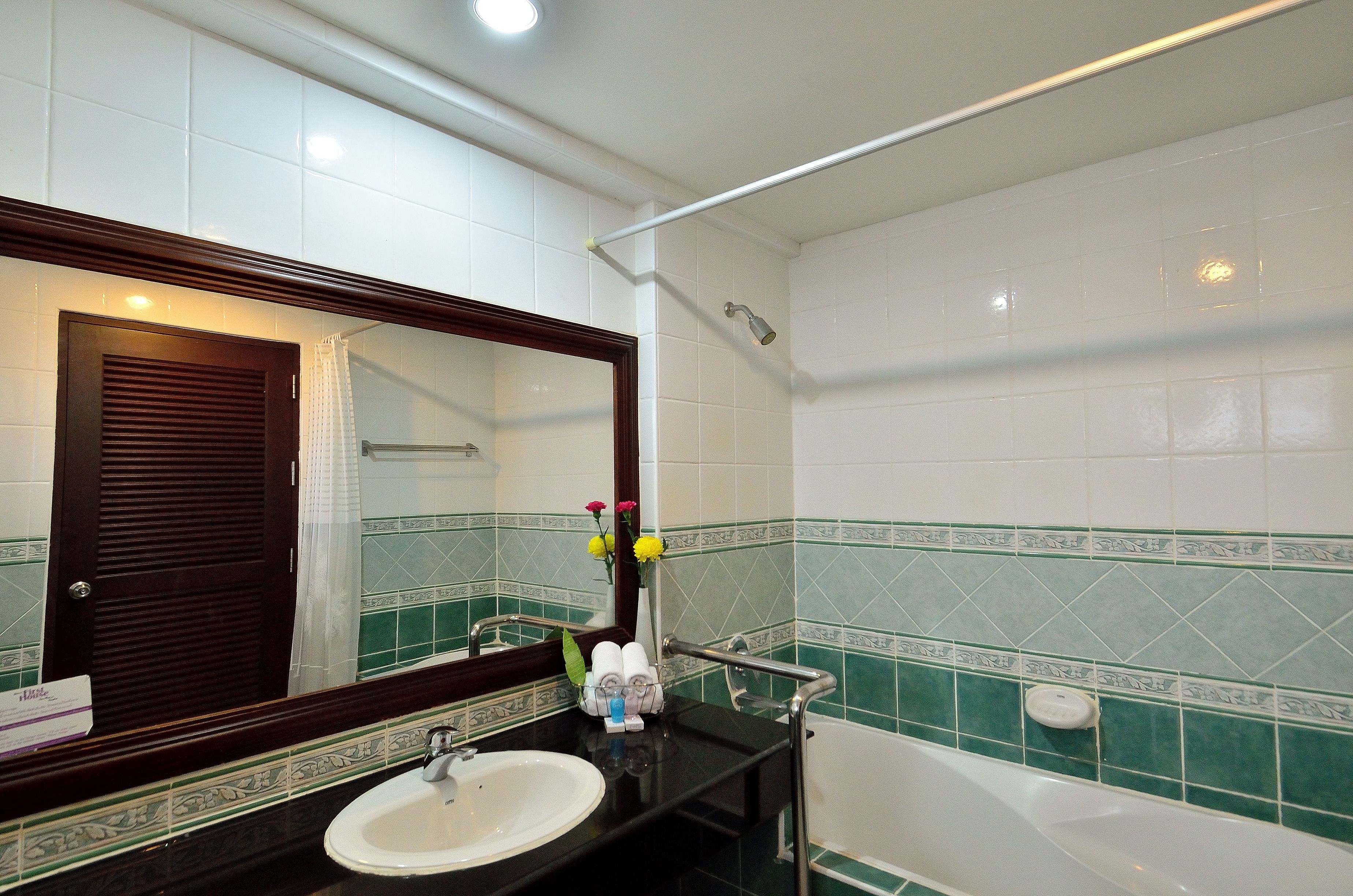 Une salle de bain avec un lavabo blanc, un miroir, une baignoire et des murs recouverts de carreaux verts.