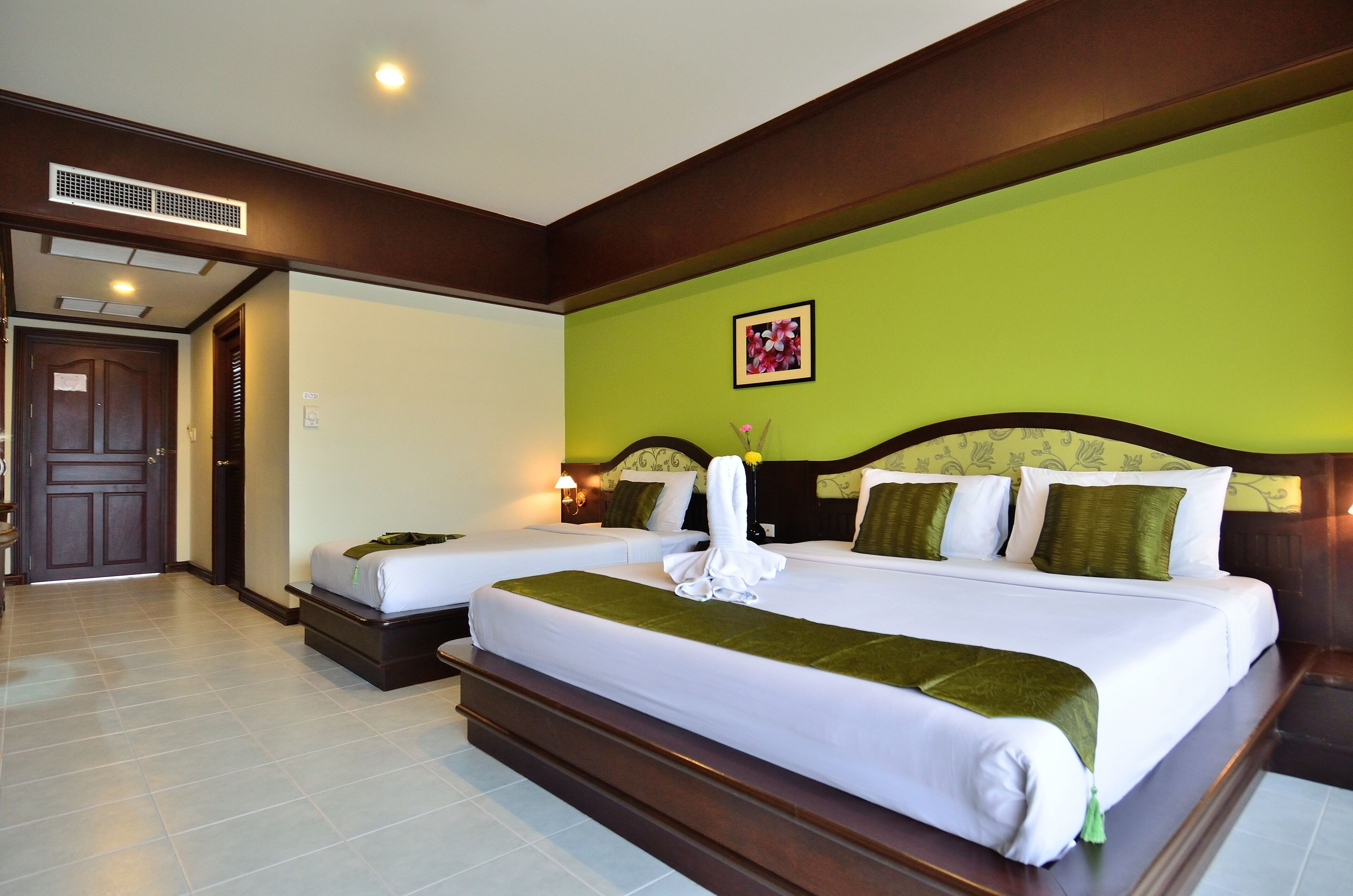 A hotel room with two beds, a green wall, and a wooden headboard.