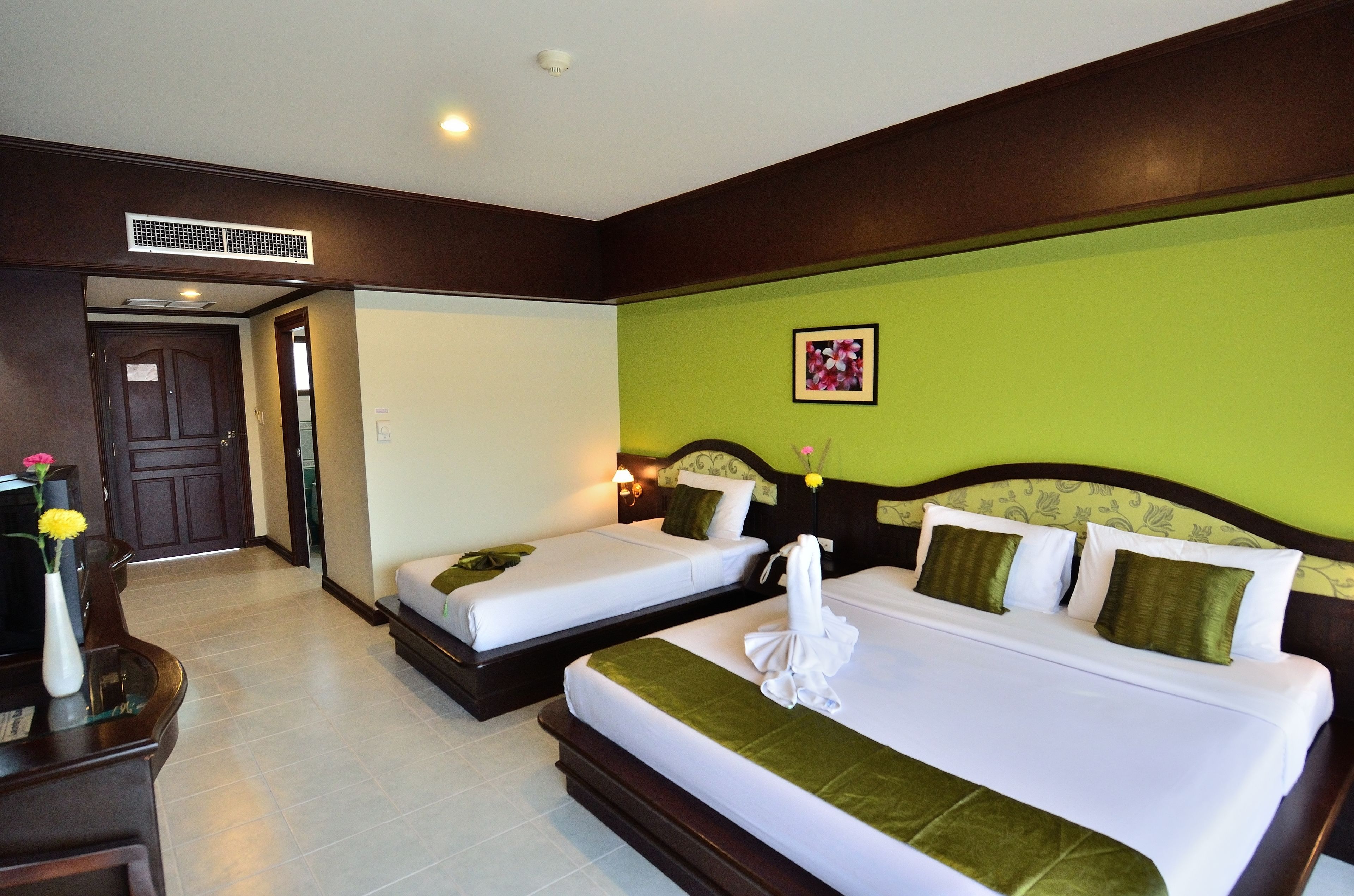 A hotel room with two beds, a desk with a vase of flowers, and a green wall.