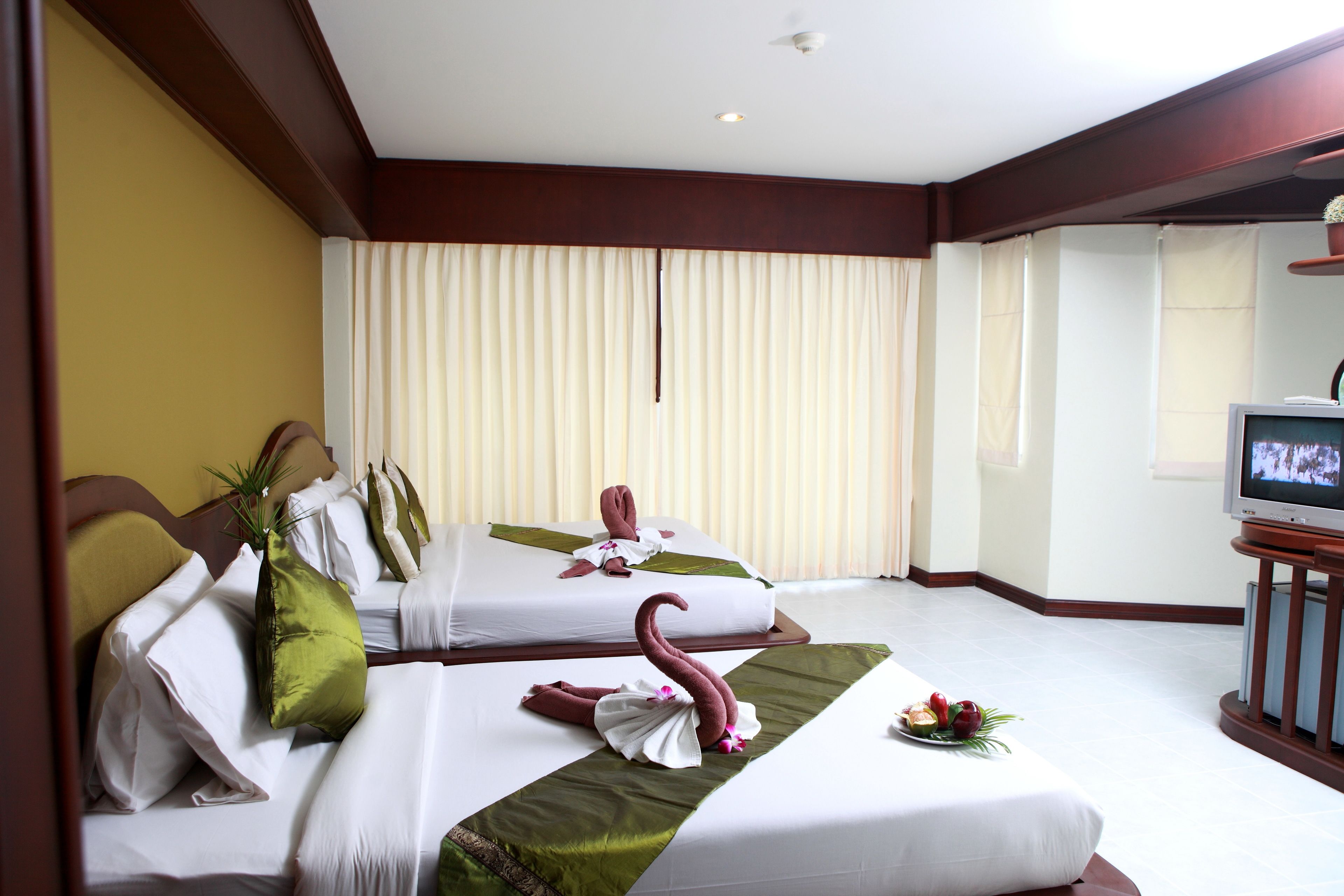 A hotel room with two beds, a television, and a large window with curtains.