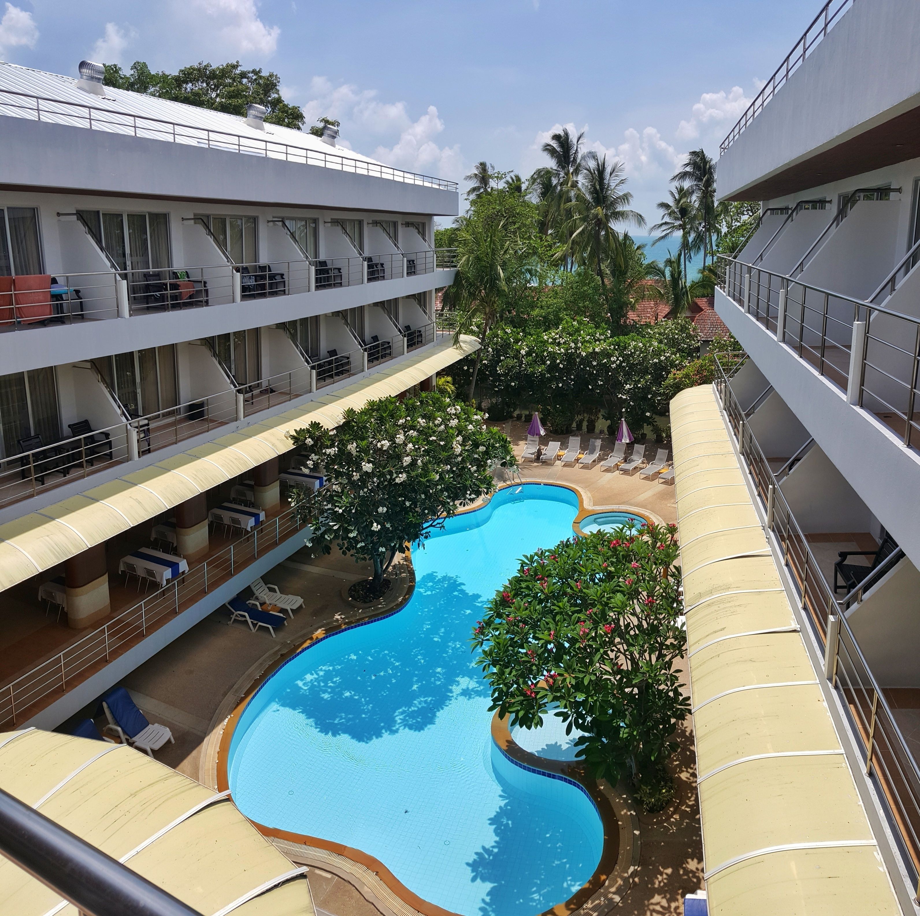 Un hotel con varios balcones, piscina y abundante vegetación.
